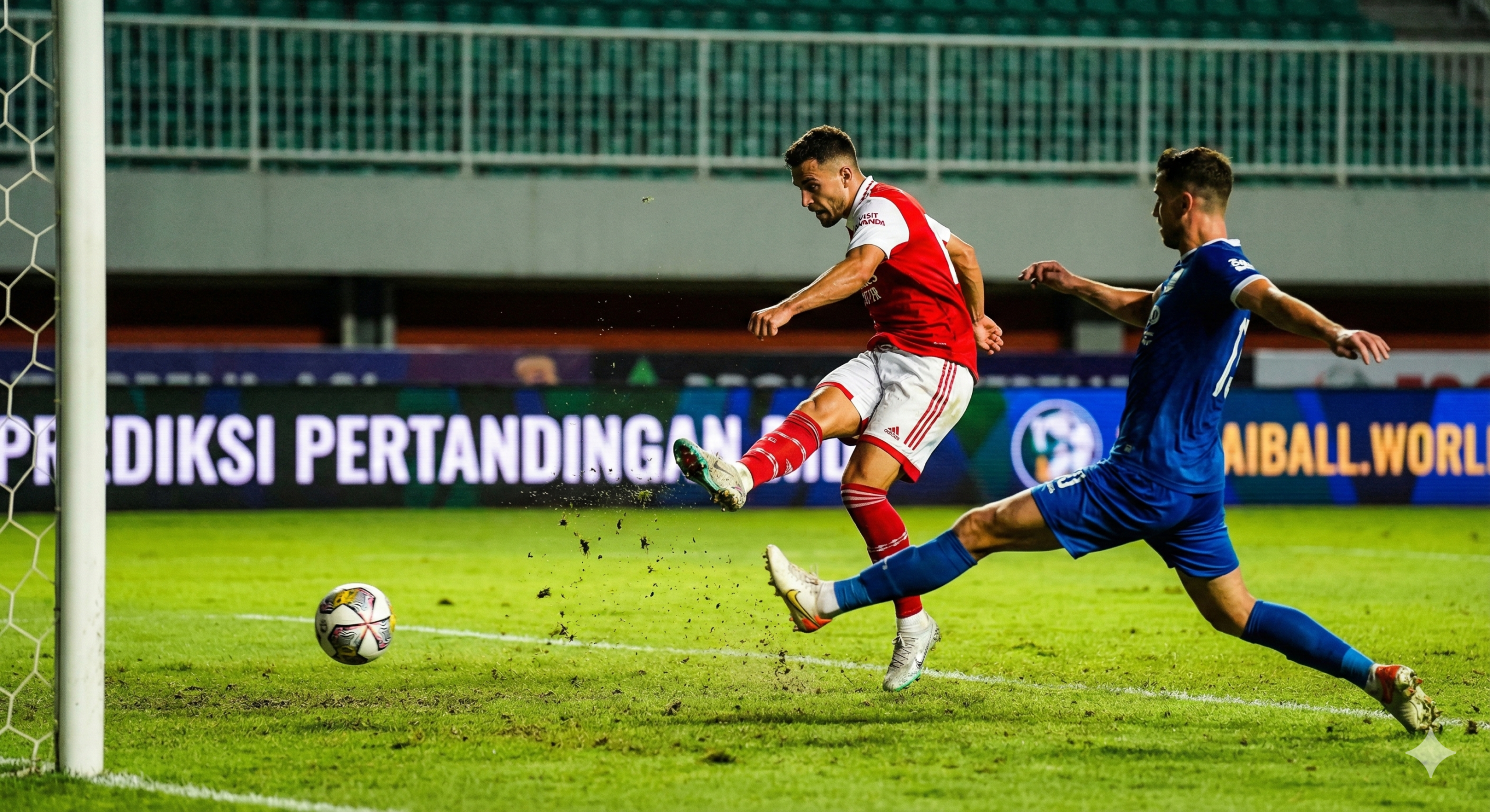 Gambar aksi sepak bola intensitas tinggi yang menangkap momen pemain berbaju merah melakukan tembakan keras di tepi kotak penalti, dengan bek berbaju biru berusaha memblokir, latar belakang stadion hijau yang buram.